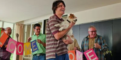 Andy Holding A Dog With People Putting A Welcome Banner Up Behind
